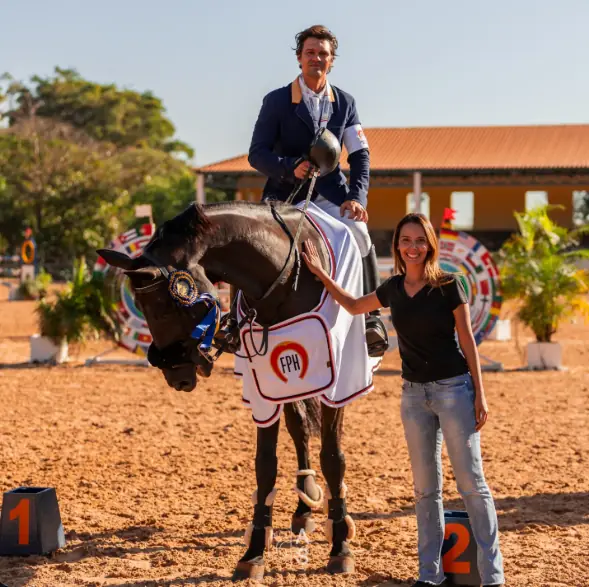 Bruno Pessanha montado em cavalo premiado, com a capa da Federação Paulista de Hipismo, ao lado de Fernanda Pessanha